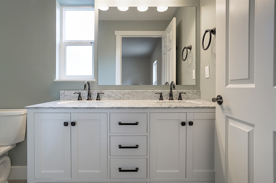 Photo of a remodeled bathroom with two sinks with dark hardware, grey and white counters and white cabinets.