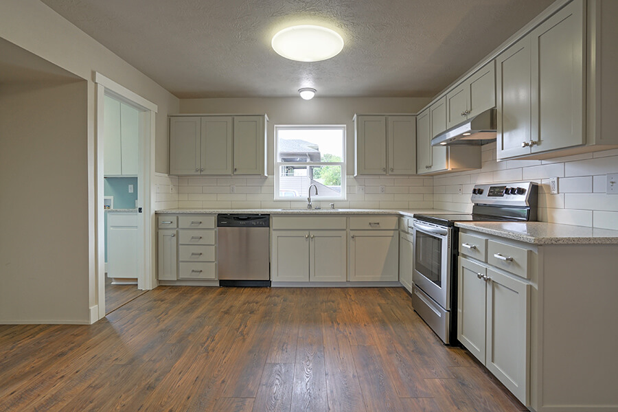 Photo of kitchen remodel with hardwood floors, beige cabinets, white backsplash and stainless steel appliances.