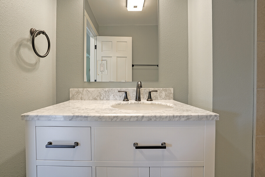 Photo of vanity remodel with grey and white marbled counter, white cabinetry and dark hardware.