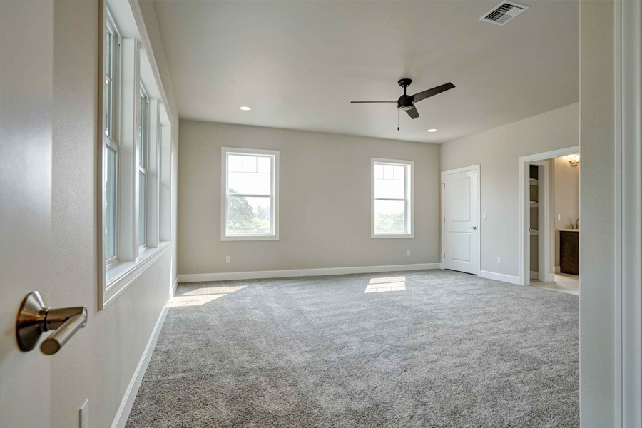 Photo of bedroom in custom home with grey carpet, white doors and windows and light tan walls.