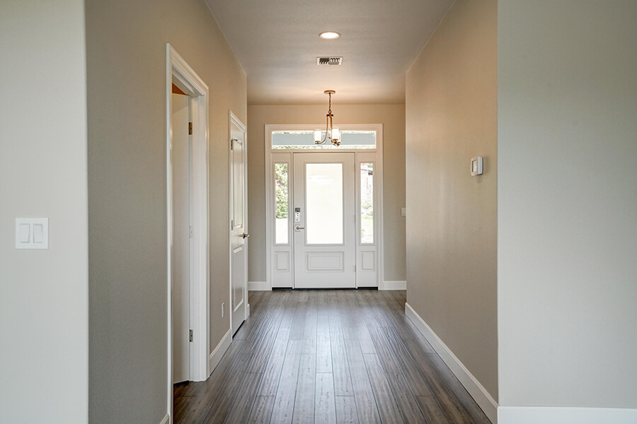 Photo of custom home foyer with glass front door and dark hardwood floors.