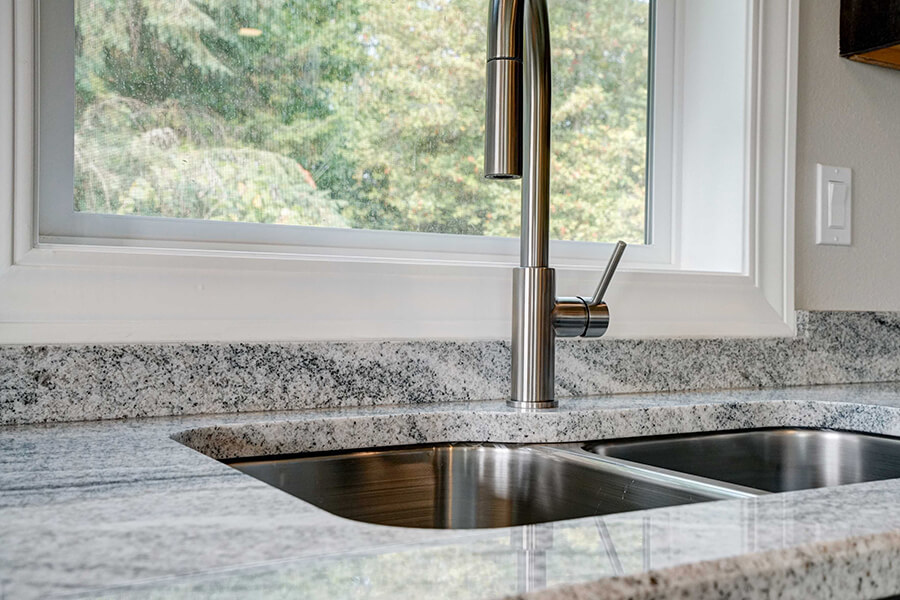 Close-up photo of an inset kitchen sink with marbled grey and white tile and silver hardware.