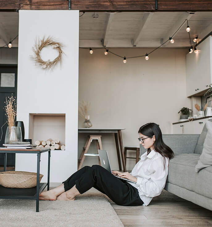 Photo of a woman sitting comfortably on the floor at home working on her laptop.