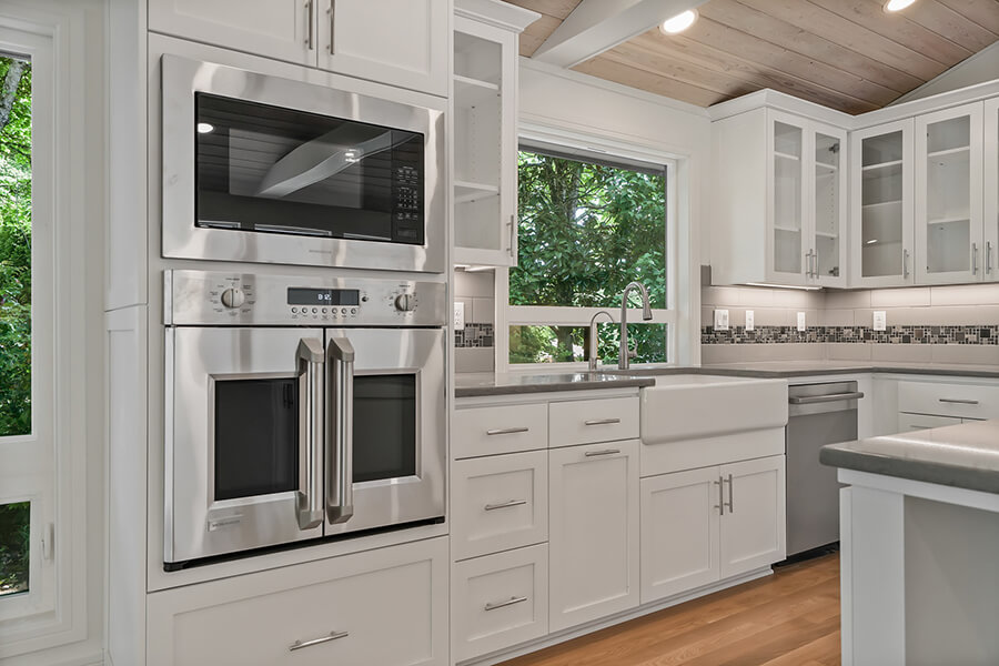 Photo of kitchen white cabinetry, double door side opening oven, microwave, sink, dishwasher and white cabinetry.