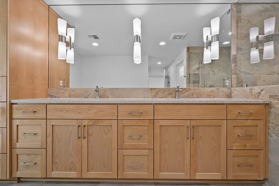 Photo of bathroom counter with two sinks, wood cabinetry and dramatic frosted glass and nickel lighting fixtures.