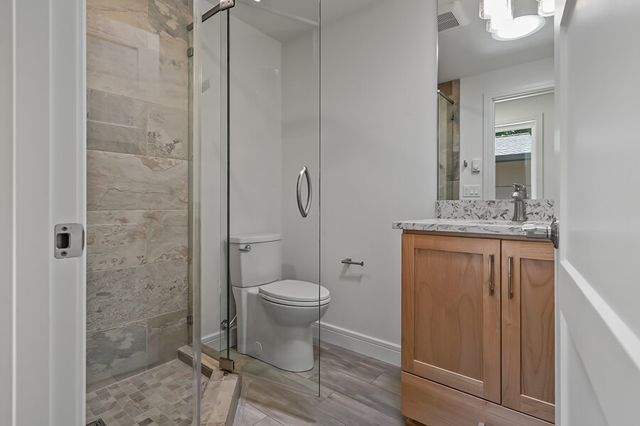 Photo of bathroom showing shower, toilet and vanity with light wood cabinetry.